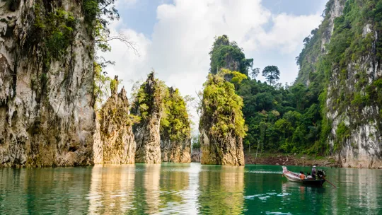 Scenic limestone cliffs and boat gliding through turquoise water in Khao Sok National Park