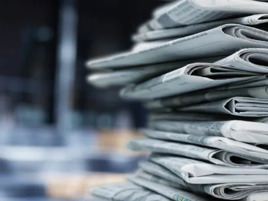 A pile of newspapers stacked on a desk.