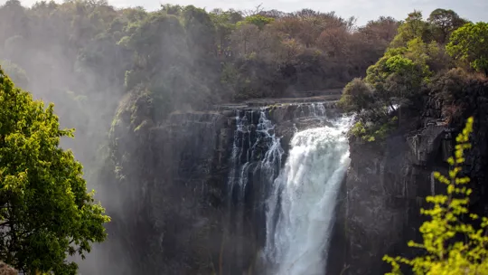 Misty waterfall cascading over rocky cliffs surrounded by lush greenery in Zambia
