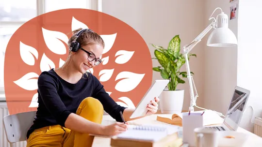 An older female student working at her desk with her laptop and reading notes she is making.