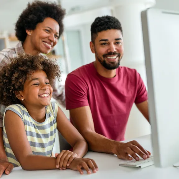 Smiling parents and child at home using a desktop computer for learning