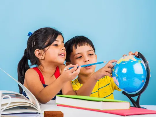 Young boy and girl looking at a globe and pointing out locations, surrounded by books