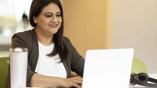 A female tutor sits at a desk, focused on her work while using a laptop computer.