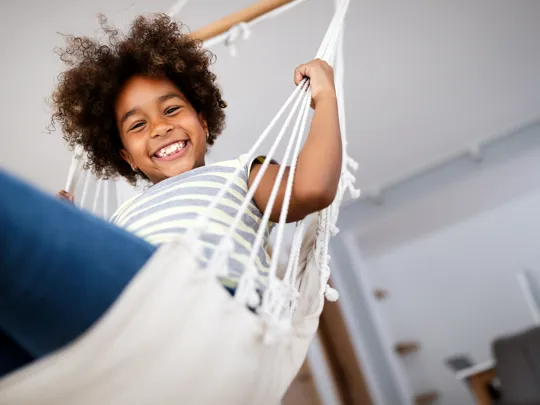 Happy child relaxing in a hammock at home, smiling confidently at the camera.