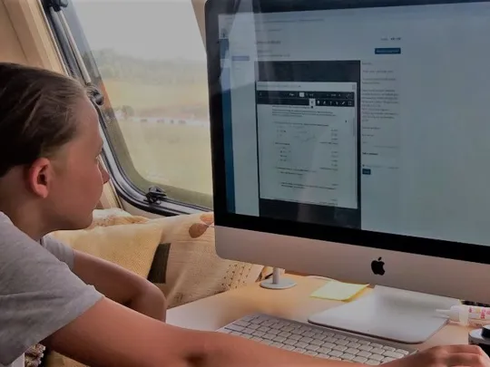 Learner engaging with online coursework on a desktop computer in a well-lit caravan setting.