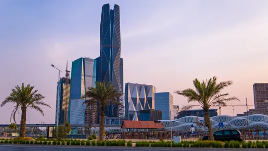 Modern skyscrapers in Riyadh, Saudi Arabia, seen from a palm-lined boulevard at sunset