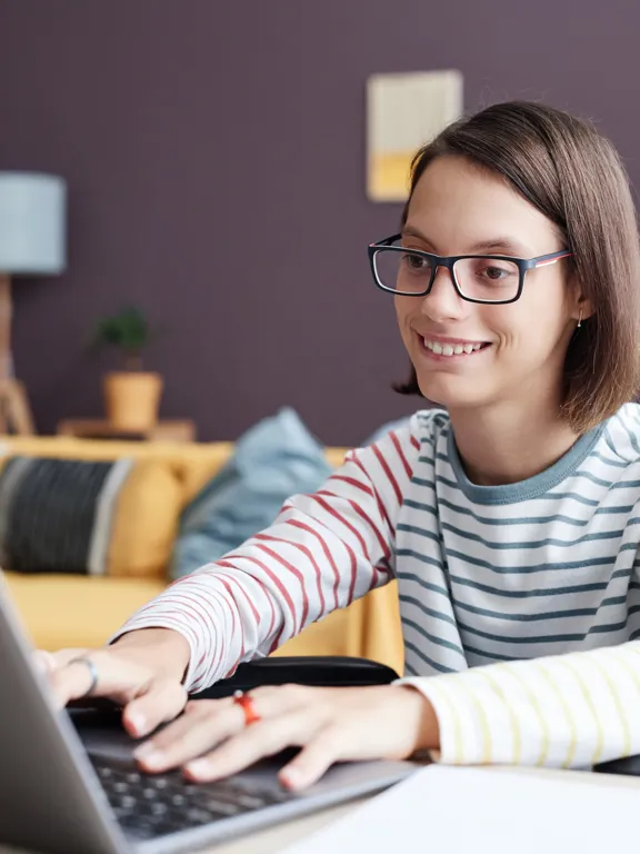 Teenage girl studying on laptop in wheelchair in comfortable home setting