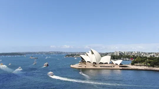 Sydney Opera House beside the harbour with boats leaving white trails in the deep blue water