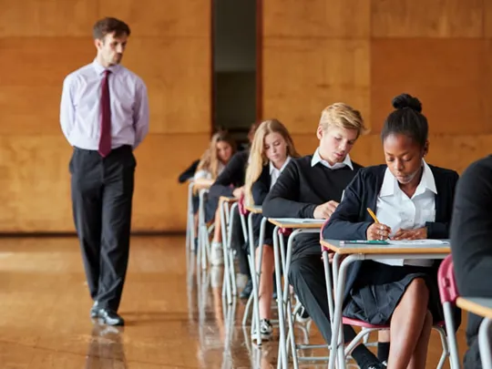 Homeschool students taking formal exams in a UK exam centre with an invigilator present.