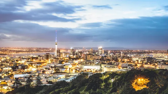 Auckland cityscape at dusk with Sky Tower lit up and reflections across the harbour