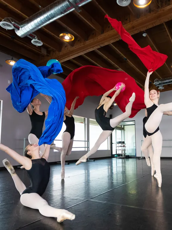 Ballet dancers mid-performance in studio with flowing red and blue fabric