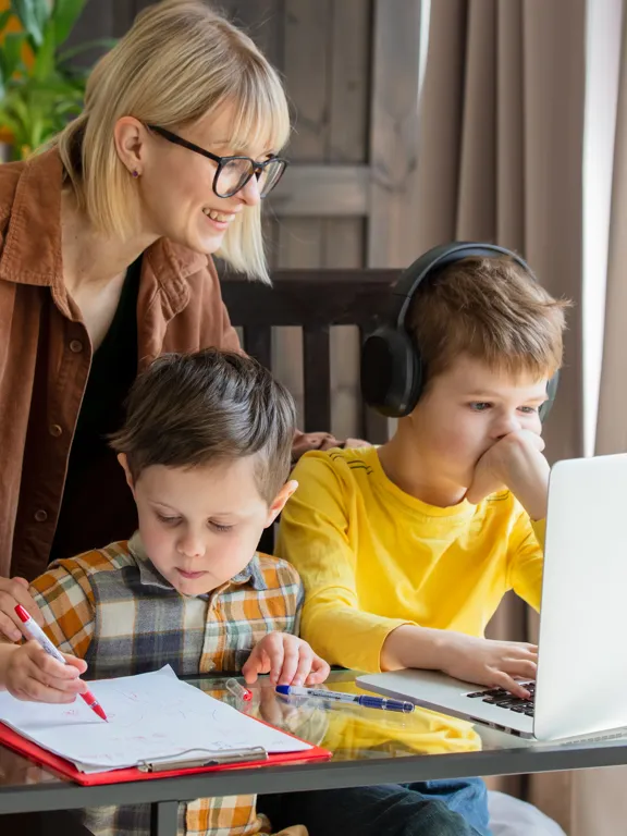 Mother guiding sons during home learning with laptop and written work