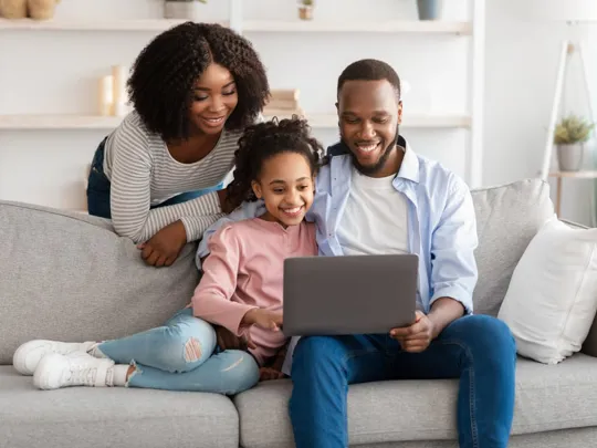 Family on couch watching a Wolsey Hall Oxford online open event on a laptop