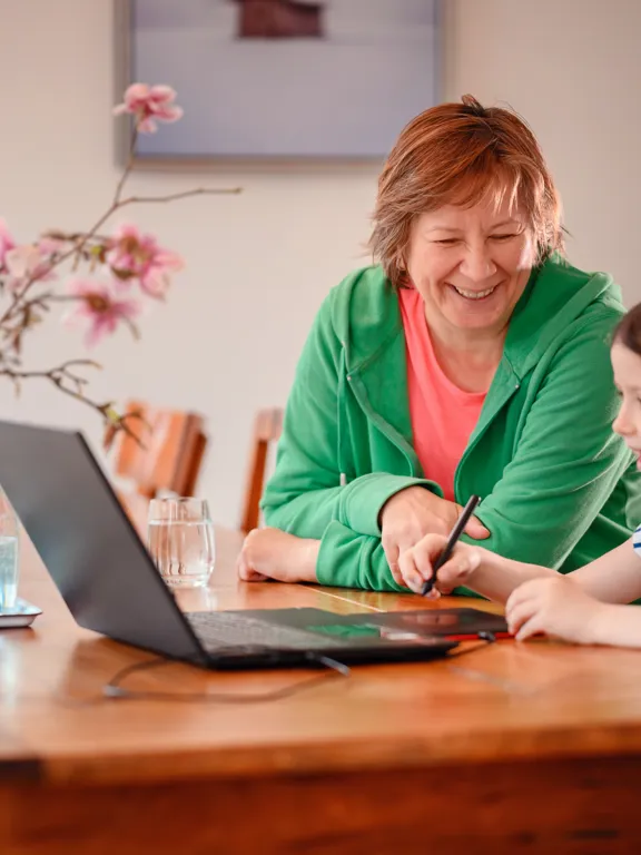 Young girl enjoying a learning activity at home with older adult and laptop