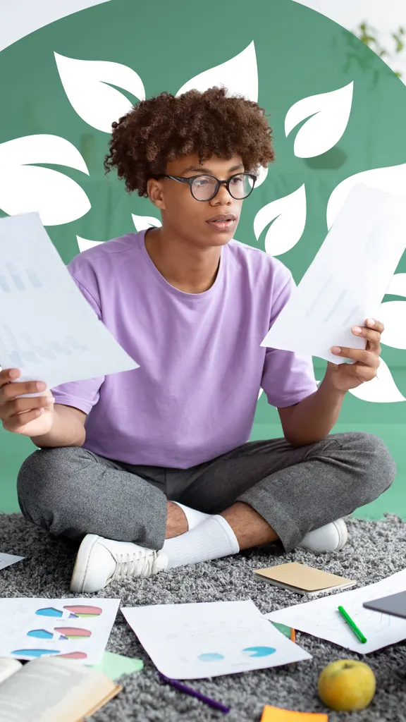 A person sitting cross-legged on a rug surrounded by study materials, holding papers and looking at a laptop, with a green leafy design in the background.