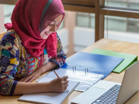 Student diligently working on her studies with a notebook and computer, representing effective homeschooling in Jeddah.