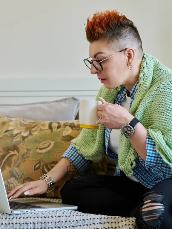 Focused parent wrapped in a blanket, holding a mug while using a laptop.