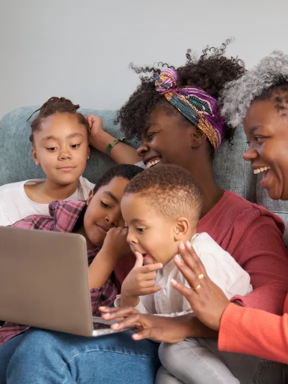Family of five sharing a moment of learning and laughter together on the sofa with a laptop.