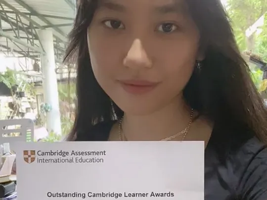 Wolsey Hall Oxford student Genie smiles at the camera holding her Outstanding Cambridge Learner Award certificate.