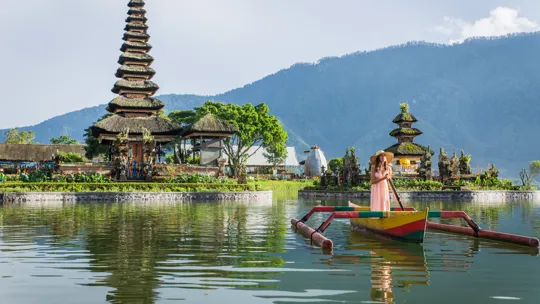 Traditional temple and colourful wooden boat on a calm lake in Bali with mountains behind