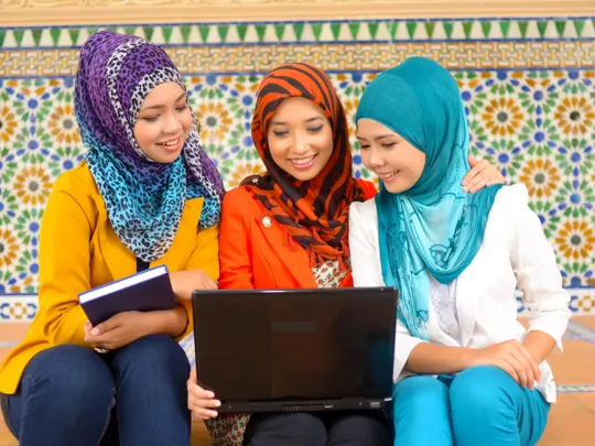 Three students happily collaborate around a laptop, showcasing a positive peer learning environment for homeschooling in Selangor.