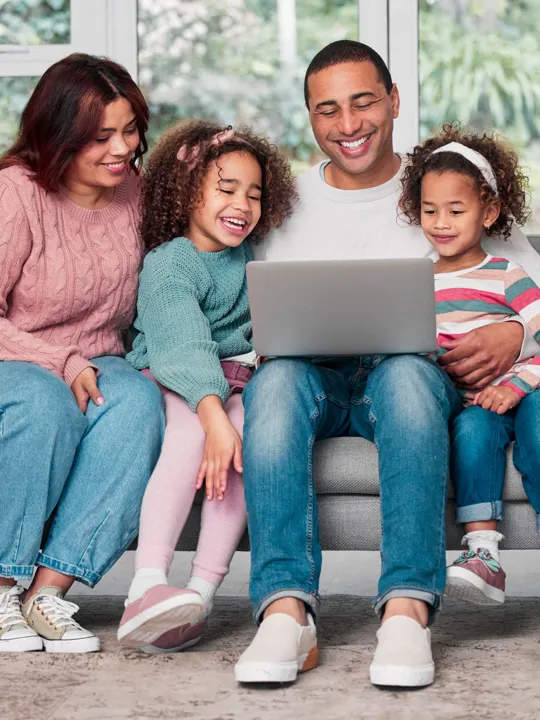 Parents and two young daughters gathered on the sofa enjoying screen time together.