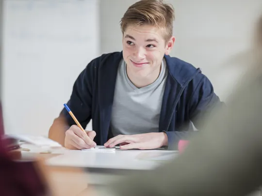 Teenage boy in casual clothing smiling while writing in a notebook during study.