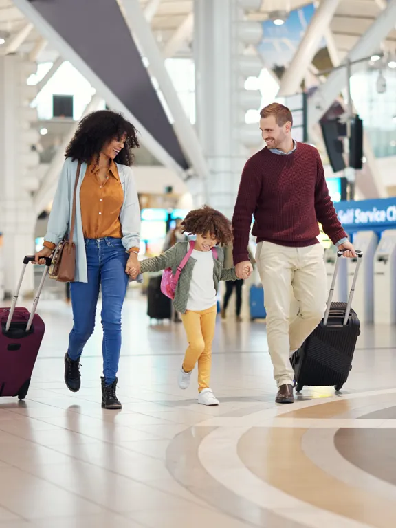 Smiling family travelling together through airport with wheeled suitcases