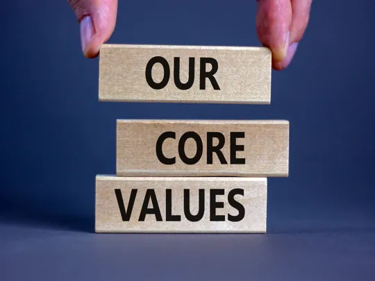 Hands stacking wooden blocks that spell out the words Our Core Values.