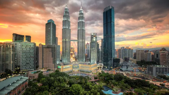 Kuala Lumpur skyline with Petronas Towers at sunset and lush city park in foreground