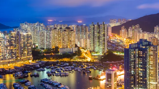 Densely packed high-rise buildings lit at night with a marina full of boats below