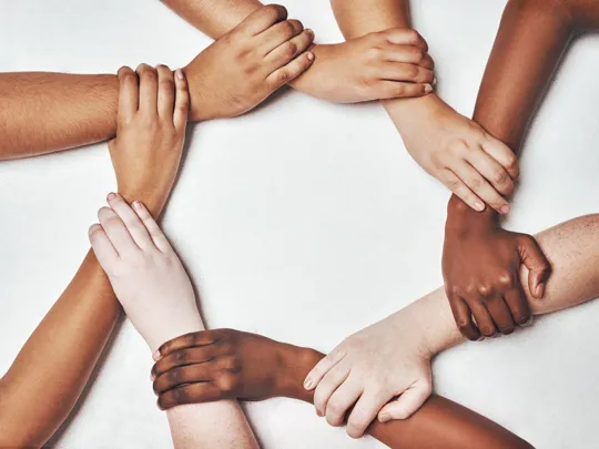 Diverse group of hands interlinked in a circle, symbolising unity and inclusion.