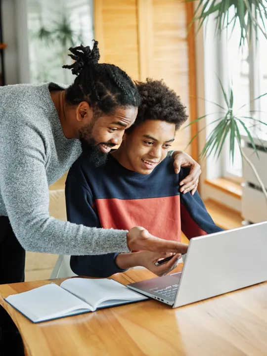 Supportive father helping his son with online learning on a laptop.